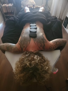 Hot stone body treatment in progress — tattooed client.